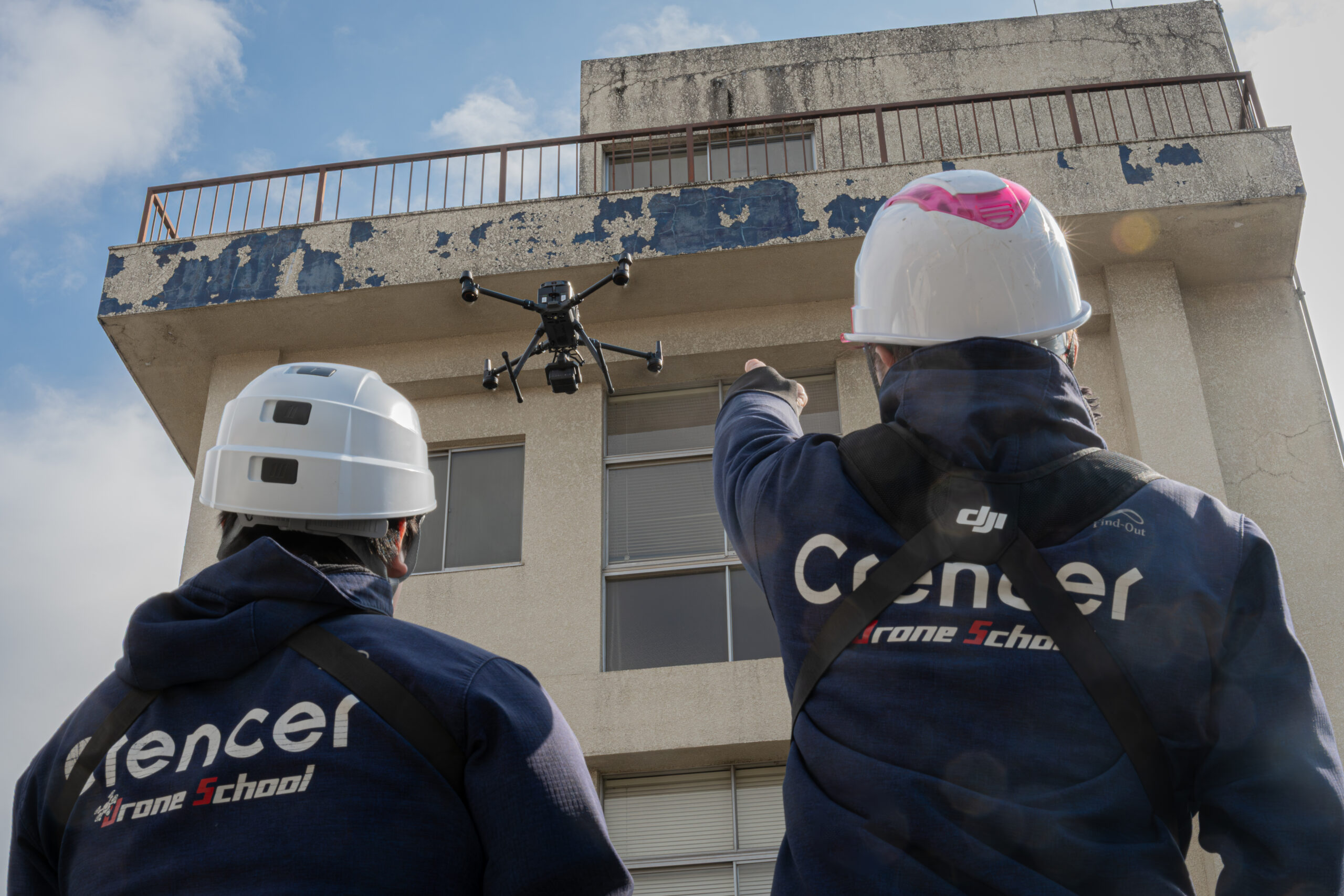 建物を見上げながらドローン飛行を確認する外壁調査写真